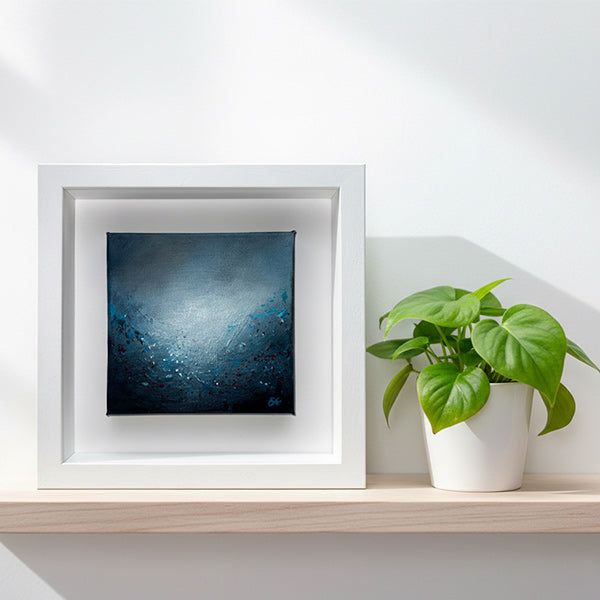 A brightly lit shelf containing Aqua Lumina I, a framed abstract painting by Sinéad Guilfoyle featuring deep blues and ethereal light. 