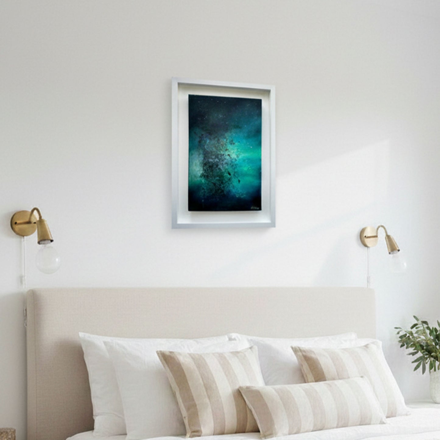 A bright, airy, and minimalist white bedroom with an abstract painting titled 'Cosmic Dust' mounted on the wall above the headboard. The painting features a composition of dark teal and midnight blue, with a radiant, explosive center of emerald green 'cosmic' particles. 