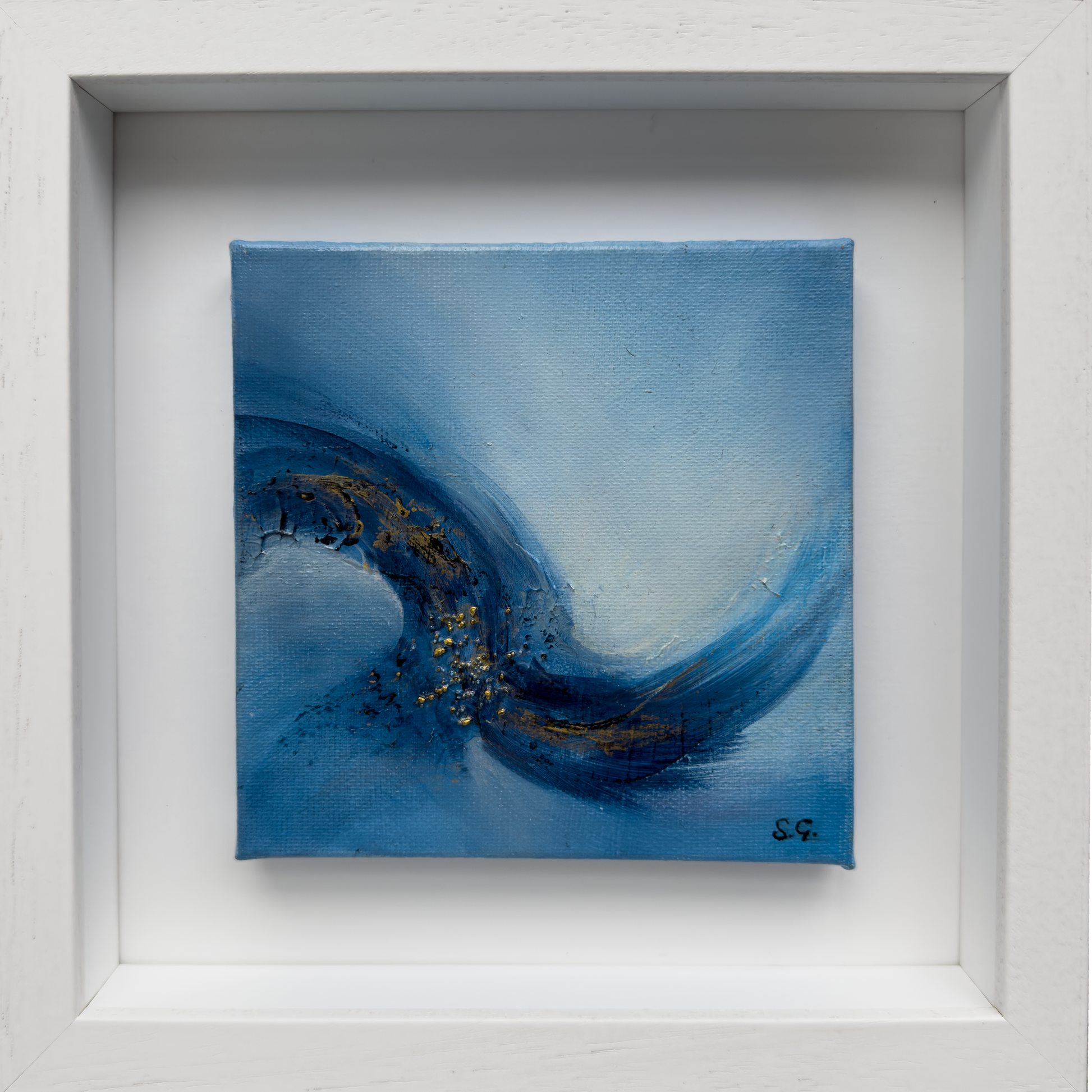 A square abstract painting, Emergence 2 by Sinéad Guilfoyle, with sweeping blue brushstrokes and gold leaf accents, titled Emergence 1, showcased in a white wooden shadow box frame.